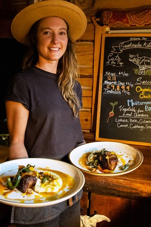 A woman holding two plates of elegantly arranged food in a restaurant with an all-wood interior.