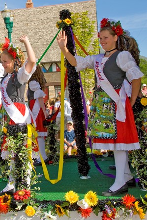 oung girls on a parade boat waving to bystanders, dressed in traditional German attire.