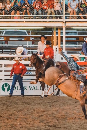 A man on a horse being bucked around in a dirt arena, with a crowd watching.