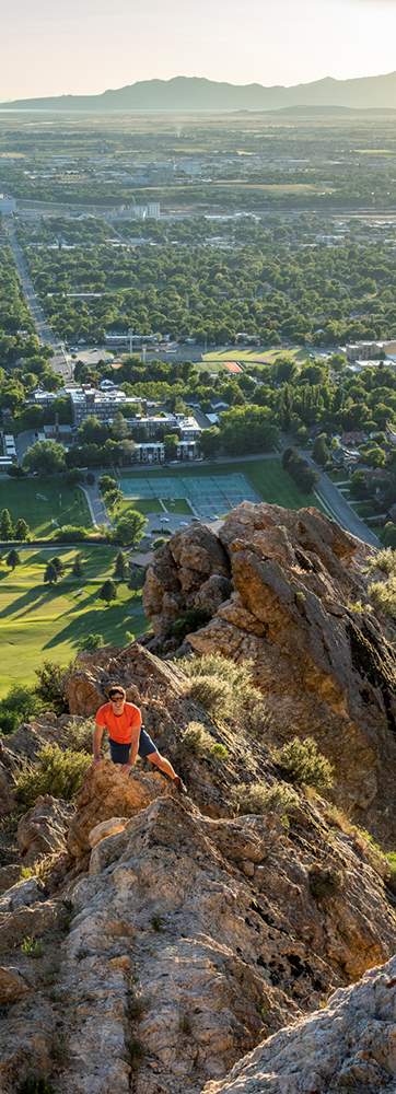 A woman standing on a mountain overlooking a valley with a city below, while a man on a lower rock level looks up at her.