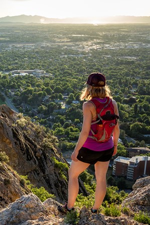 A woman standing on a mountain overlooking a valley with a city below, while a man on a lower rock level looks up at her.