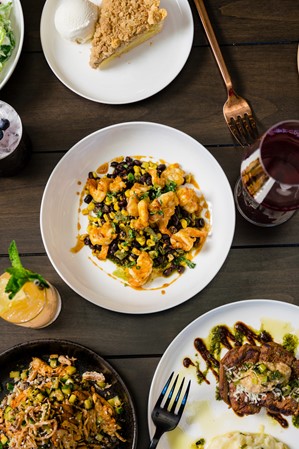 An aerial shot of dishes arranged on a table, including roasted carrots, pie, steak, salad, and biscuits.